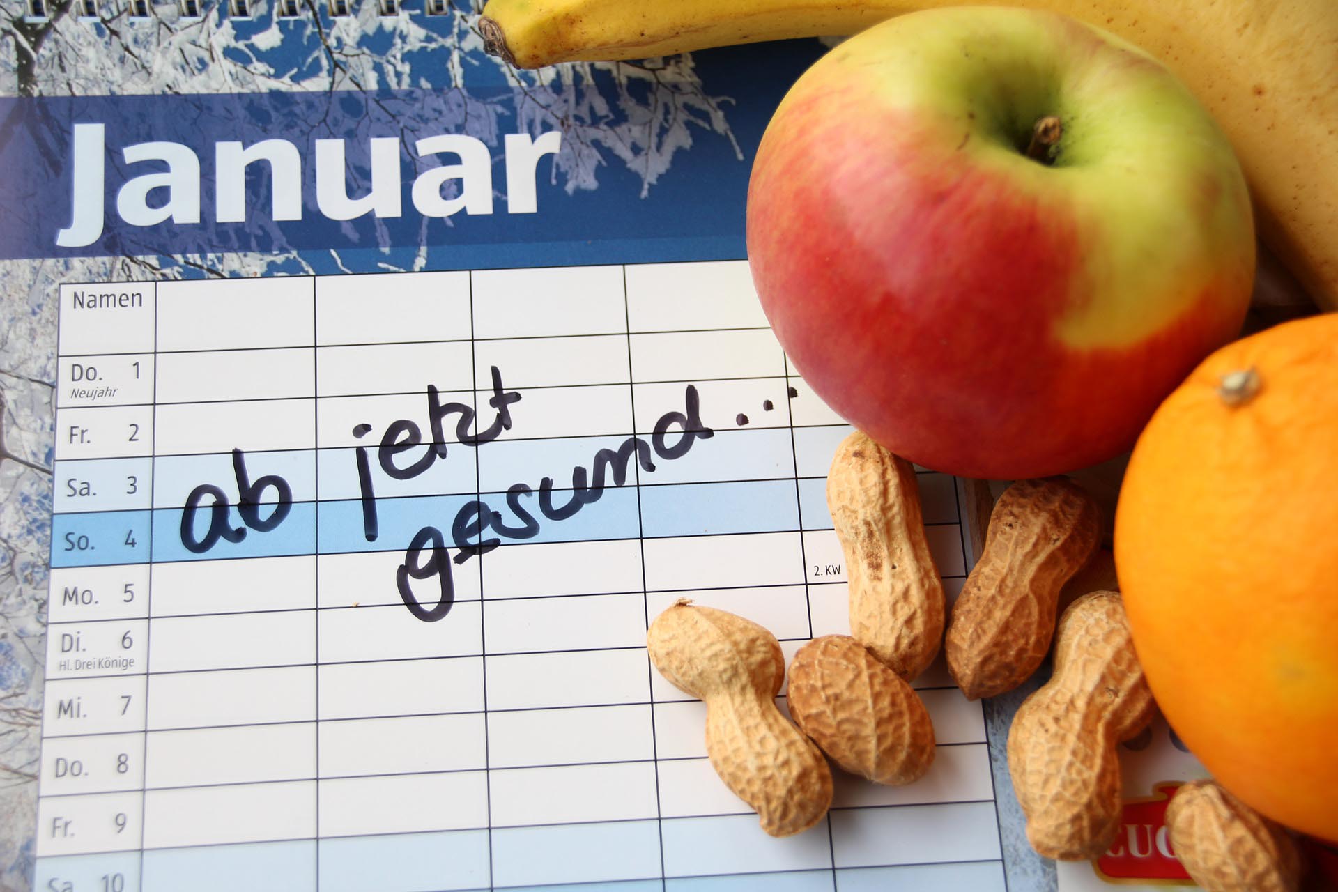 Ein Taschenkalender im Hintergrund. Davor liegen auf der rechten Seite Erdnüsse und ein Apfel.